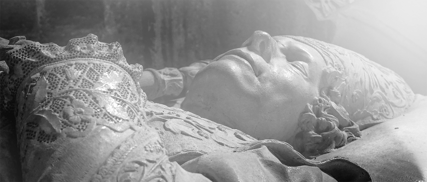 Black and White photography of a sculpture of a dead man laying on a bed in a Cathedral